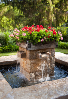 Small square water fountain with four spouts and flowers on top.