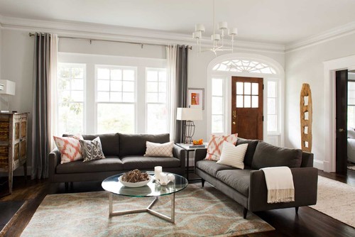 A living room with two gray couches sitting perpendicular to one another with a round glass top coffee table in the middle